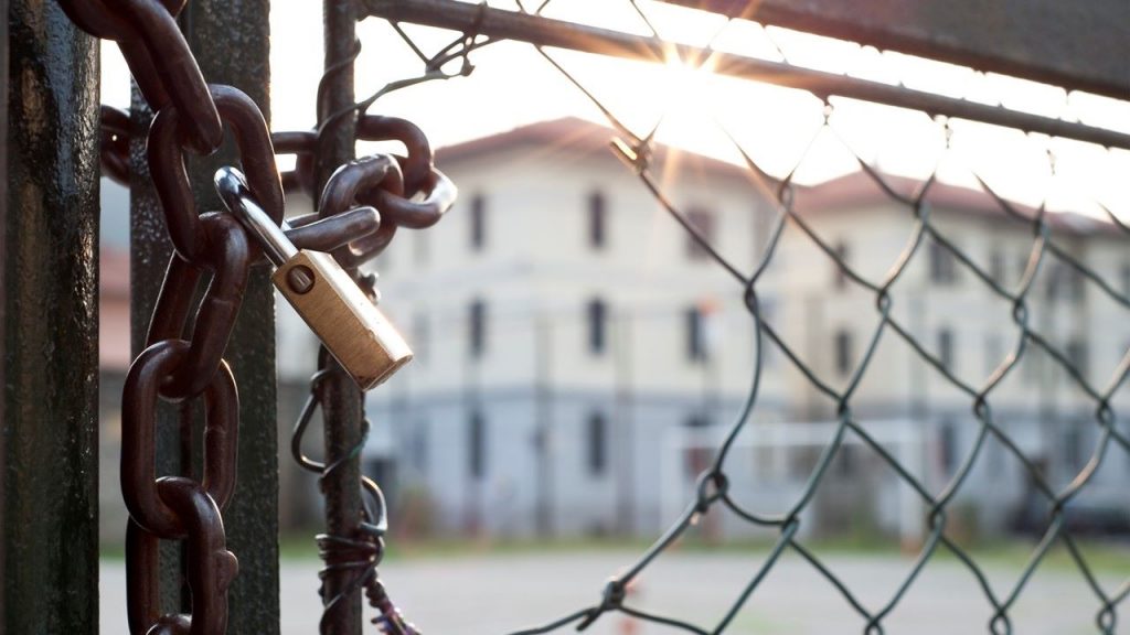 Picture of a locked gate with a hole in the fence next to the lock