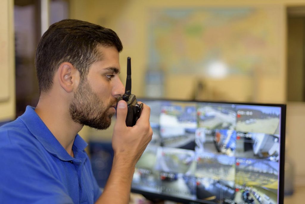 security person talking on walkie talkie while viewing security footage