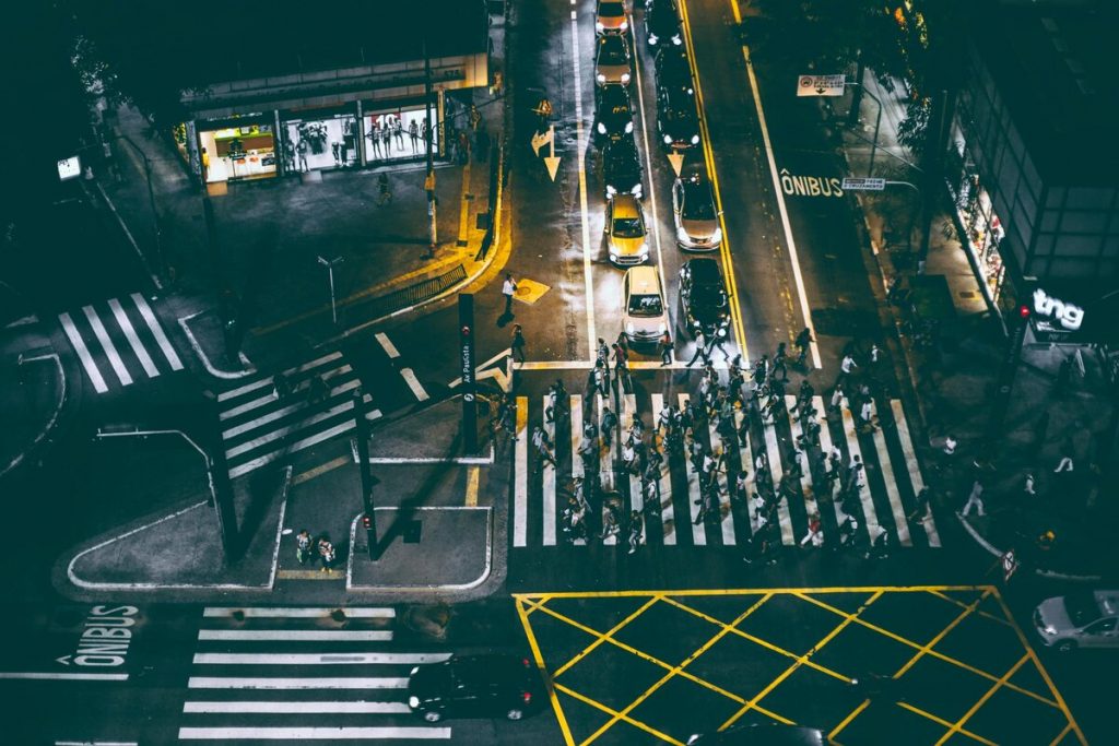 Aerial view of urban intersection at night with pedestrians crossing, illustrating pattern of life analysis and human movement tracking for corporate security intelligence.