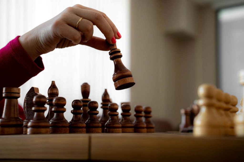 A hand moves a wooden chess piece across a board, symbolizing careful strategy and decision-making.